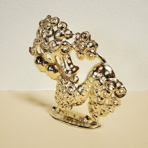 Op de afbeelding: Een gouden metalen beeldje van een leeuw met ingewikkelde details en een decoratieve basis.