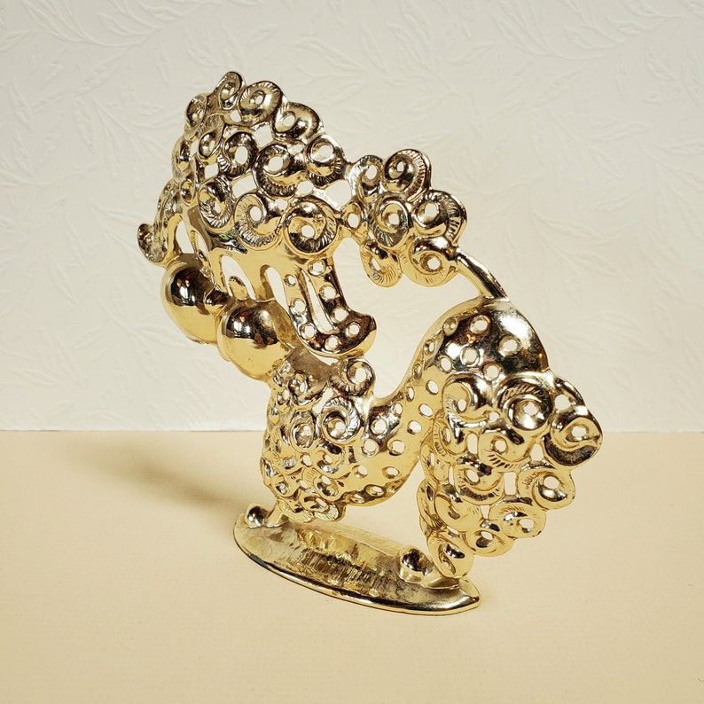 Op de afbeelding: Een gouden metalen beeldje van een leeuw met ingewikkelde details en een decoratieve basis.
