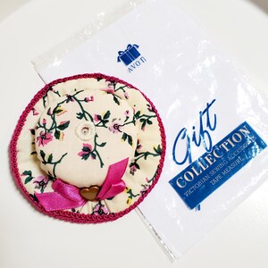 May include: A hat-shaped floral pin cushion with a pink bow and trim. The pin cushion is part of the Avon Gift Collection, which includes Victorian sewing accessories and a tape measure.