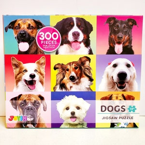May include: A jigsaw puzzle box featuring nine different dog breeds against colorful backgrounds. The puzzle contains 300 pieces and measures 29 inches by 21.5 inches. The box has the word "DOGS" and "JIGSAW PUZZLE" printed on it.