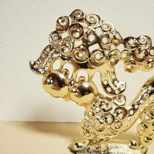 Op de afbeelding: Een gouden metalen beeldje van een gestileerde draak met ingewikkelde details. De draak is opgerold met zijn kop omhoog en zijn staart om zijn lichaam gewikkeld. Het beeldje is gemaakt van massief metaal en heeft een gladde, gepolijste afwerking.