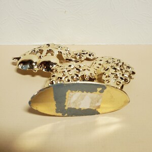 Op de afbeelding: Goudkleurige metalen servetthouder in de vorm van een gestileerde pauw met een decoratieve basis.