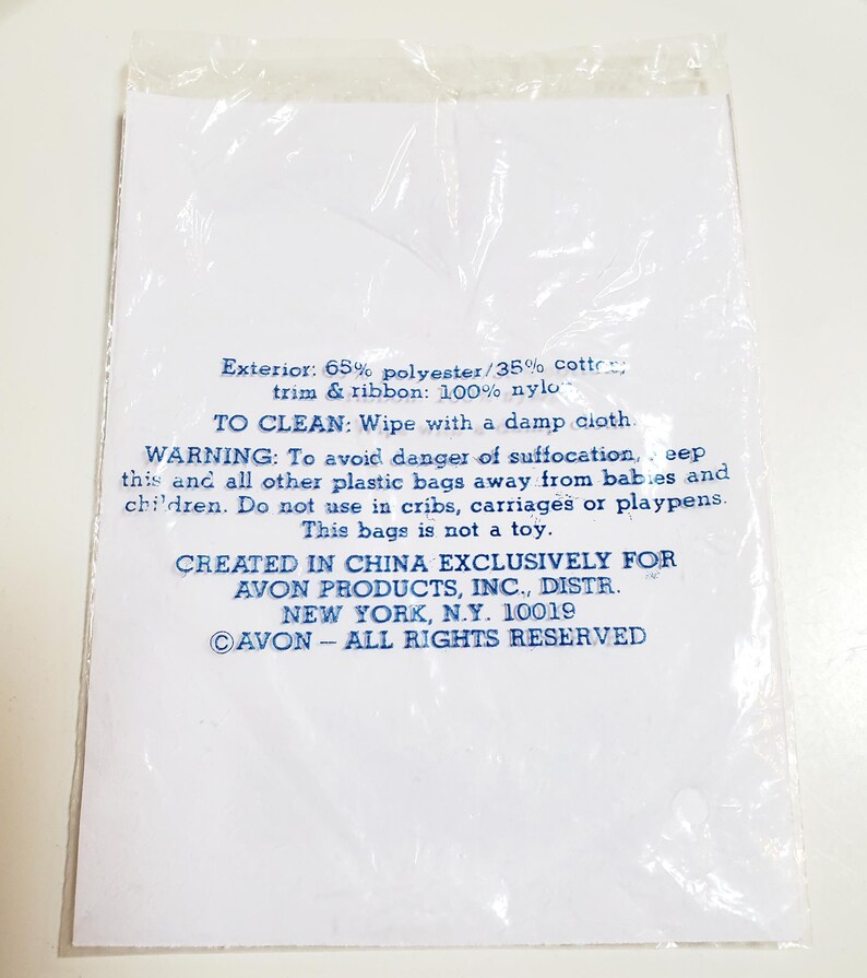 May include: A white paper insert with blue text inside a clear plastic bag. The text includes cleaning instructions, a warning about suffocation, and the phrase "CREATED IN CHINA EXCLUSIVELY FOR AVON PRODUCTS, INC."