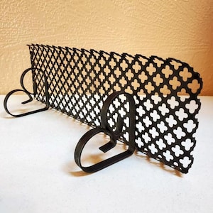 May include: Black metal decorative shelf with a quatrefoil pattern. The shelf has two heart-shaped supports. The shelf is designed to hold books or display items. The shelf is made of metal and has a matte finish.