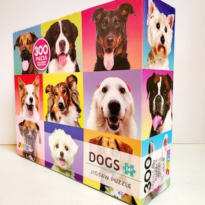 May include: A colorful jigsaw puzzle box featuring portraits of various dog breeds. The box displays the word "DOGS" and indicates it contains 300 pieces. The puzzle dimensions are 29 in x 21.5 in (73.66 cm x 54.61 cm).