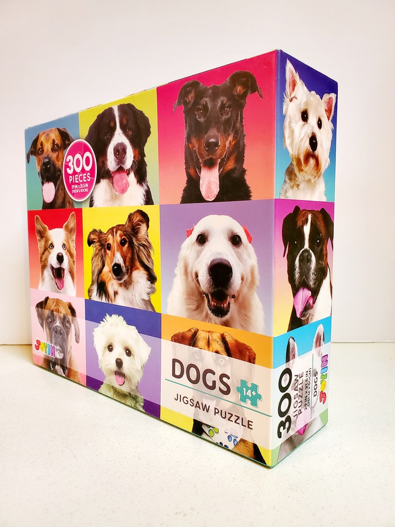 May include: A colorful jigsaw puzzle box featuring portraits of various dog breeds. The box displays the word "DOGS" and indicates it contains 300 pieces. The puzzle dimensions are 29 in x 21.5 in (73.66 cm x 54.61 cm).