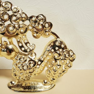 Op de afbeelding: Een gouden metalen decoratief beeldje van een gestileerde draak met ingewikkelde details. De draak staat op een voetstuk en heeft een cirkelvormig ontwerp over zijn hele lichaam.
