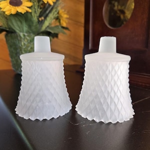May include: Two white frosted glass candle holders with a diamond pattern. The holders are made of glass and have a frosted finish.