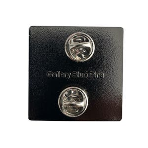 Back of hard enamel pin with two vertical pin posts and back stamp.