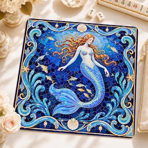 Könnte beinhalten: Eine quadratische Dekormatte mit einer Mosaik-Illustration einer Meerjungfrau mit langem rotem Haar, umgeben von blauem Wasser, kleinen gelben Fischen und Muscheln. Der Rand ist mit komplizierten blauen und goldenen Wirbelmustern verziert.