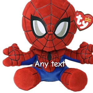 May include: A plush Spider-Man doll in a seated position. The doll is primarily red with black web detailing and blue accents. The eyes are white with black outlines. The doll has a Ty heart-shaped tag. The text "Any text" is visible.