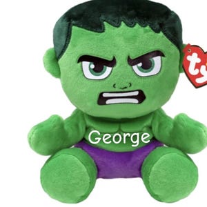 May include: A green plush toy of the Hulk character with a stern expression. The toy has black hair, white teeth, and purple shorts. The name "George" is printed on the chest. A red heart-shaped tag is attached.