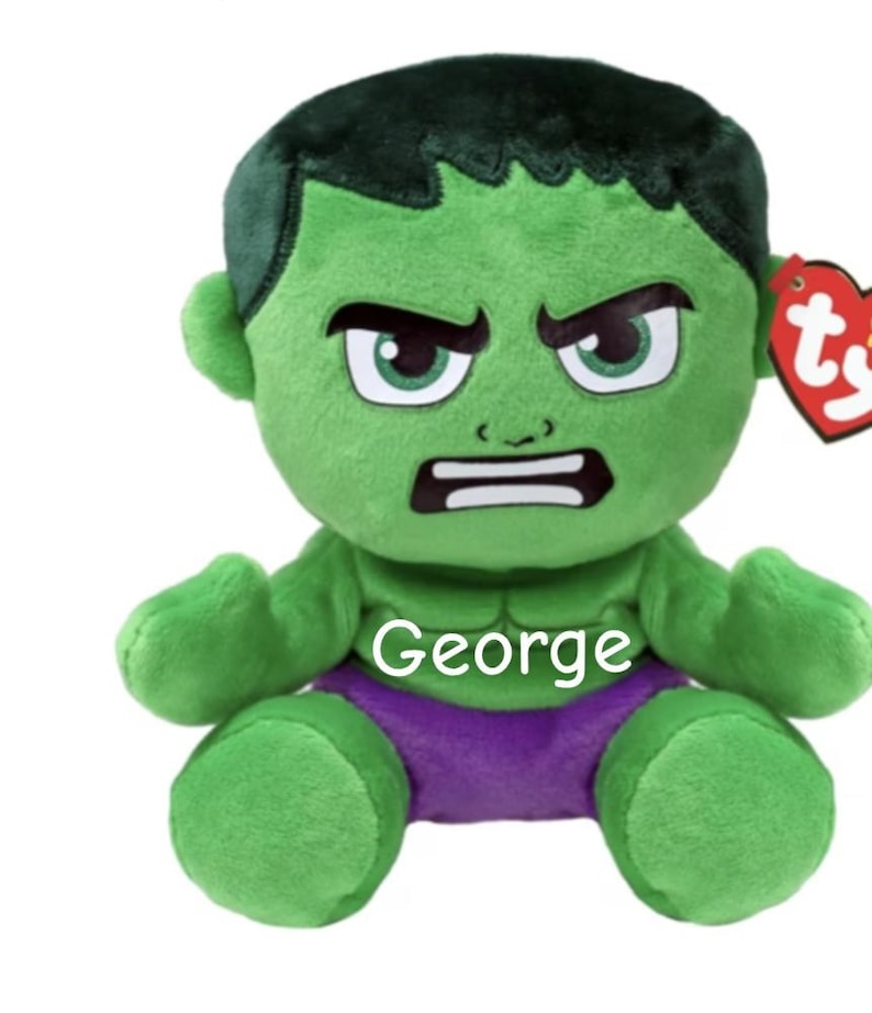 May include: A green plush toy of the Hulk character with a stern expression. The toy has black hair, white teeth, and purple shorts. The name "George" is printed on the chest. A red heart-shaped tag is attached.
