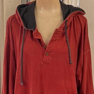 May include: A red hooded shirt with a gray hood lining and drawstrings. The shirt has a button-down placket and long sleeves. The fabric appears to be a soft, casual material.