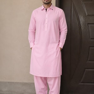 May include: A light pink long-sleeved kurta with a classic collar and a buttoned placket, paired with matching loose-fitting trousers. The garment features a dark purple inner collar lining and is worn with dark brown slip-on leather shoes.