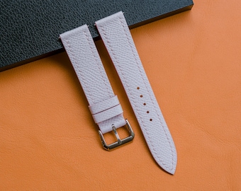 Peut inclure: Un bracelet de montre rose clair avec une surface texturée et des coutures ton sur ton. Le bracelet comporte deux passants coulissants et une boucle en métal argenté poli. L'extrémité longue présente cinq trous de réglage et une pointe.