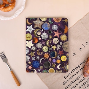 May include: A purple notebook cover adorned with celestial imagery, including moons, stars, and suns in various colors and designs. The cover features a collage of whimsical illustrations, creating a mystical and artistic aesthetic.