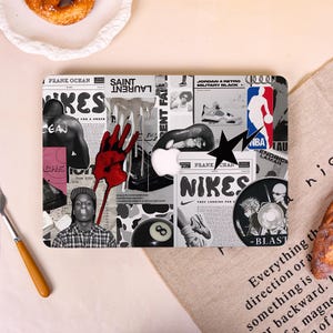 May include: A rectangular laptop case with a collage design featuring black and white images, red accents, and text. The design includes a red hand, a black star, and the word "NIKES".