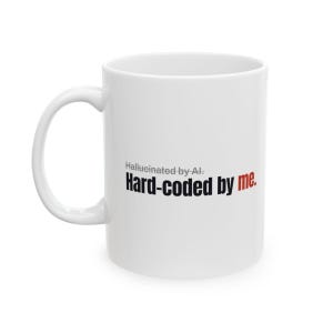 Op de afbeelding: Een witte keramische mok met een handvat aan de linkerkant. De tekst op de mok luidt Hallucinated by AI. in kleine grijze letters, met de woorden Hard-coded by me. eronder gedrukt in grotere zwarte en rode tekst, waarbij me in het rood staat.