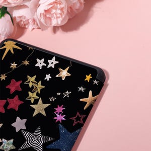May include: Black phone case with a colorful star design. The case features various star shapes in gold, red, white, and other colors. The stars are scattered across the black surface, creating a celestial theme.
