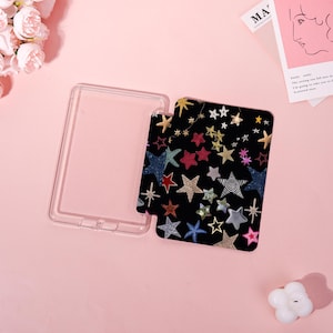 May include: A clear, rectangular phone case with a black insert featuring a colorful star pattern. The stars are in various colors and designs, including gold, red, blue, and silver, against a black background. The case is open, showing the insert.