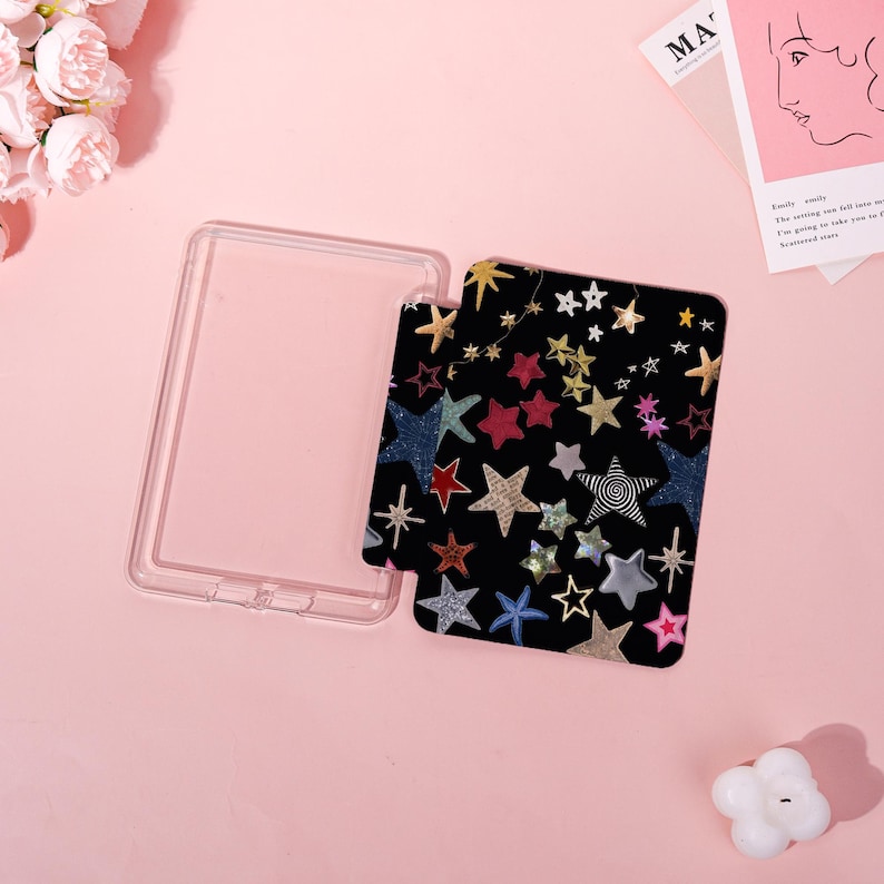 May include: A clear, rectangular phone case with a black insert featuring a colorful star pattern. The stars are in various colors and designs, including gold, red, blue, and silver, against a black background. The case is open, showing the insert.