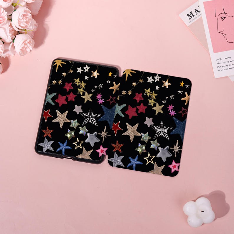 May include: Two black tablet cases with a colorful star pattern. The stars are in various colors, including gold, red, blue, and silver. Some stars have a patterned design. The cases are on a pink surface.