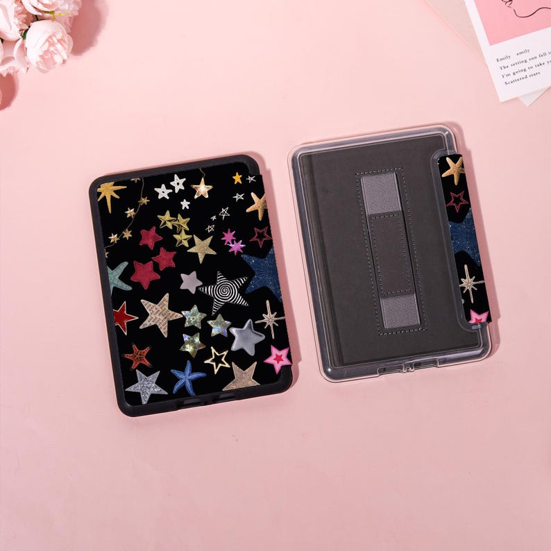 May include: Black tablet case with a colorful star pattern. The case features stars in various colors and textures, including gold, red, and silver. A clear protective case is next to it, with a matching star-patterned hand strap.