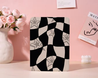 May include: A rectangular object featuring a black and white chequered pattern with grey stars. The design is on a rectangular object, possibly a tablet case or decorative item. The background is a soft pink.