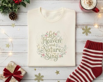 May include: A cream-coloured t-shirt featuring the text "Let Heaven and Nature Sing" within a floral wreath. The image includes festive decorations: a red and white striped sock, a gift, and a mug of hot chocolate.