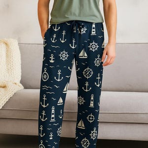 Op de afbeelding: Marineblauwe pyjamabroek met een nautisch patroon met ankers, zeilboten, stuurwielen en vuurtorens. De broek heeft een taille met trekkoord. De persoon op de afbeelding draagt een groen t-shirt.