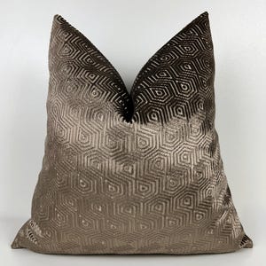 May include: A decorative pillow with a geometric pattern. The pillow features a gradient of brown tones, transitioning from a lighter shade at the bottom to a darker shade at the top. The pattern is a repeating hexagonal design.