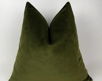 May include: Olive green velvet pillow. The square pillow has a soft, plush texture and a deep, rich color. The pillow is a solid color and has a simple, elegant design. The pillow is a decorative item for a bed or sofa.