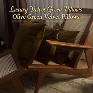 May include: Olive green velvet pillows rest on a wooden chair with a woven back. The pillows are square and plush, with a luxurious sheen. The text in the image reads "Luxury Velvet Green Pillows" and "Olive Green Velvet Pillows".