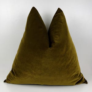 May include: Two olive green velvet throw pillows against a white background. The pillows are triangular in shape, with a soft, plush texture. The color is a deep, rich shade of green, adding a touch of luxury to any space.
