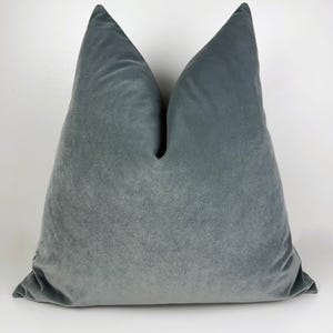 May include: A large, square, teal-colored velvet pillow. The pillow has a soft, plush appearance and is likely used for decorative purposes on a bed or sofa. The pillow is a solid color and has a simple, elegant design.