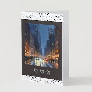 Könnte beinhalten: Grußkarte mit einem Aquarellgemälde einer Stadtstraße in der Abenddämmerung. Das Bild ist in einem schwarzen Rahmen mit drei weißen Herzen am unteren Rand eingefasst. Die Karte hat einen weißen Hintergrund mit schwarzen Sprenkeln.
