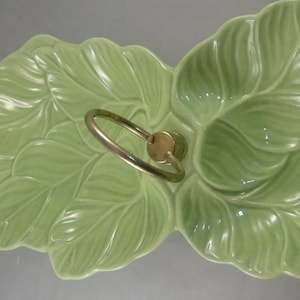 May include: A green ceramic serving dish shaped like leaves with a gold metal handle. The dish has two sections and is perfect for serving snacks or appetizers.