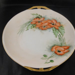 May include: A white porcelain serving plate with a gold rim and two handles. The plate features a hand-painted design of orange poppies and green leaves.