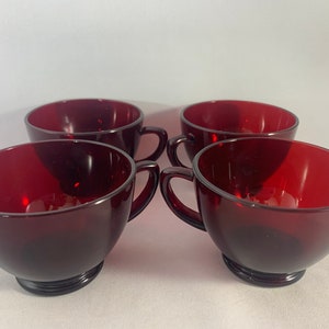 May include: Set of four red glass teacups with handles. The cups are round and have a slight curve to the bottom.