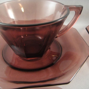 K&ouml;nnte beinhalten: Ein Set aus zwei amethystfarbenen gl&auml;sernen Teetassen und Untertassen. Die Tassen und Untertassen sind achteckig und haben einen Vintage-Look.