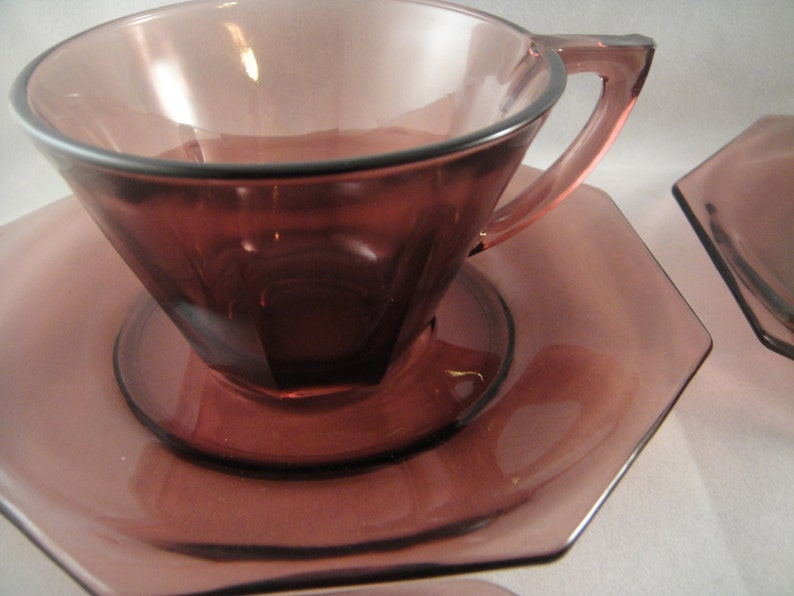 K&ouml;nnte beinhalten: Ein Set aus zwei amethystfarbenen gl&auml;sernen Teetassen und Untertassen. Die Tassen und Untertassen sind achteckig und haben einen Vintage-Look.