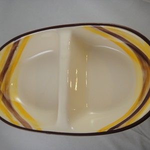 May include: A divided serving dish with a white background and brown and yellow stripes. The dish is oval shaped and has a divided center.