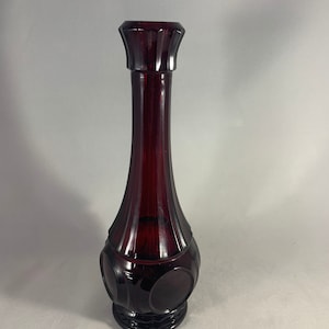 May include: A dark red glass vase with a round base and a flared top. The vase has a textured surface and a circular design.