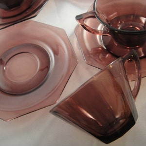 K&ouml;nnte beinhalten: Set aus vier Amethyst-Glas-Teetassen und Untertassen. Die Tassen und Untertassen haben eine achteckige Form und eine glatte, gl&auml;nzende Oberfl&auml;che.