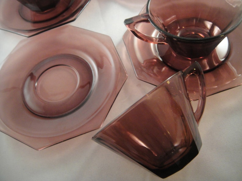 K&ouml;nnte beinhalten: Set aus vier Amethyst-Glas-Teetassen und Untertassen. Die Tassen und Untertassen haben eine achteckige Form und eine glatte, gl&auml;nzende Oberfl&auml;che.