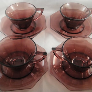K&ouml;nnte beinhalten: Set aus vier Amethyst-Glas-Teetassen und Untertassen. Jede Tasse und Untertasse hat ein geometrisches Design.