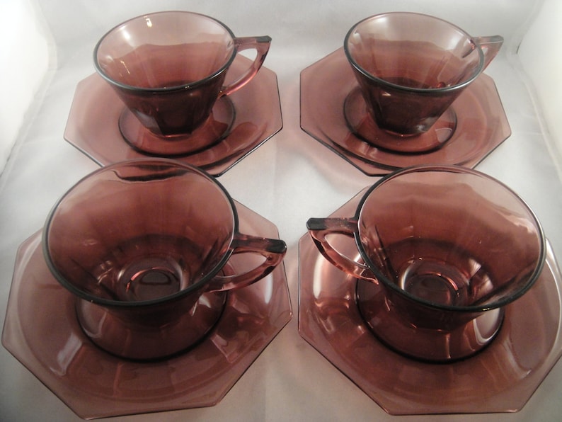 K&ouml;nnte beinhalten: Set aus vier Amethyst-Glas-Teetassen und Untertassen. Jede Tasse und Untertasse hat ein geometrisches Design.