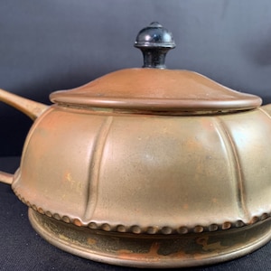 May include: A vintage, gold-toned teapot with a black knob on the lid. The teapot has two handles and a beaded rim.