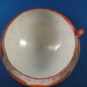 May include: A white teacup and saucer with a floral design in shades of pink and orange. The saucer has a scalloped edge.